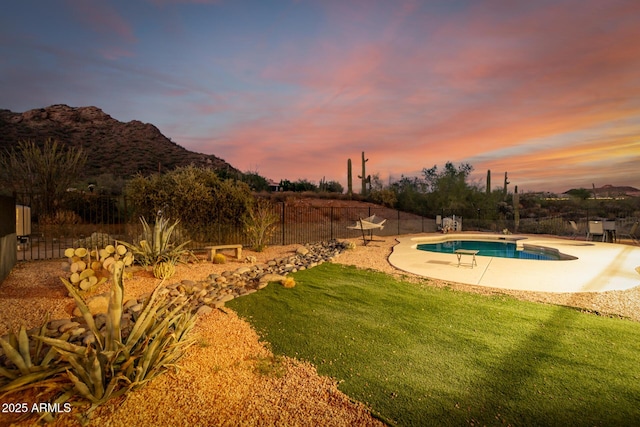 pool at dusk featuring a mountain view and a lawn