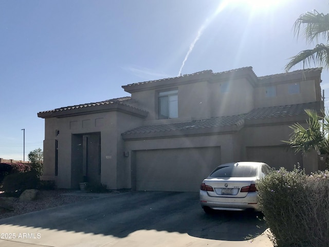 mediterranean / spanish-style house featuring a garage, driveway, a tiled roof, and stucco siding