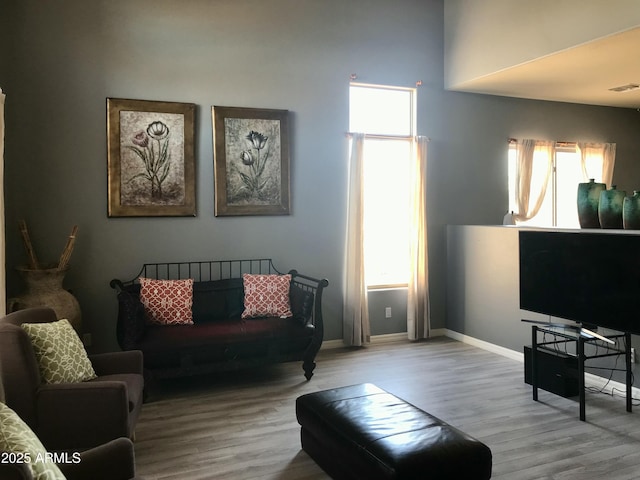 living area with visible vents, a towering ceiling, baseboards, and wood finished floors