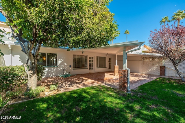 rear view of house featuring stucco siding, a lawn, a ceiling fan, a patio area, and fence