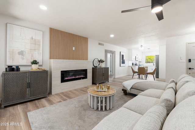 living room with visible vents, a ceiling fan, a glass covered fireplace, wood finished floors, and recessed lighting