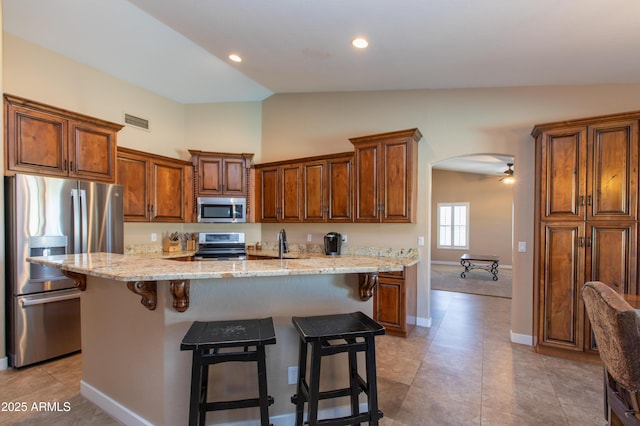 kitchen featuring lofted ceiling, a kitchen island with sink, appliances with stainless steel finishes, and a breakfast bar area