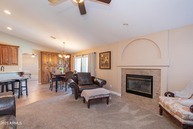 living room with ceiling fan with notable chandelier, light colored carpet, a tile fireplace, and vaulted ceiling