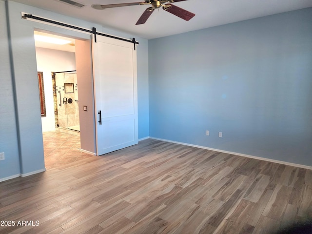 unfurnished bedroom with light wood-style floors, a barn door, baseboards, and a ceiling fan