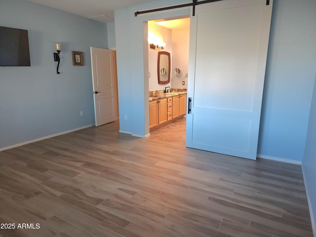 unfurnished bedroom featuring light wood finished floors, a barn door, baseboards, and a sink