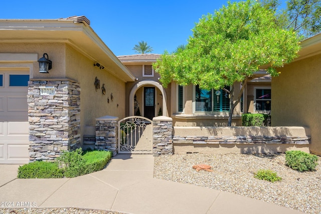 doorway to property with a gate, an attached garage, and stucco siding