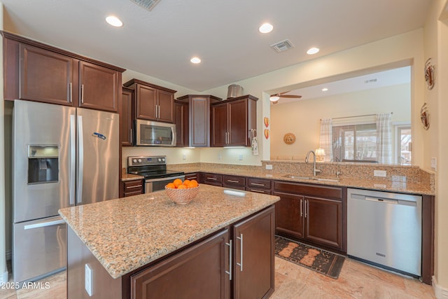 kitchen featuring sink, a center island, stainless steel appliances, light stone countertops, and dark brown cabinets