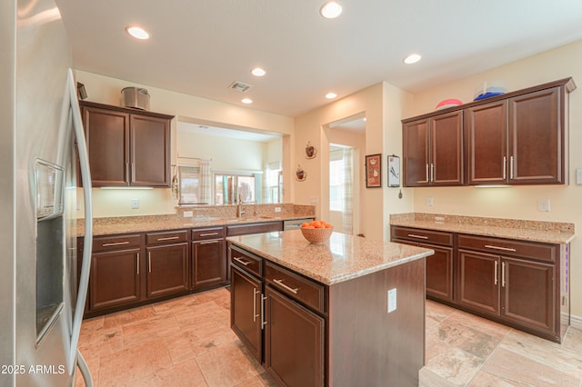 kitchen with light stone counters, stainless steel fridge with ice dispenser, dark brown cabinets, and a center island