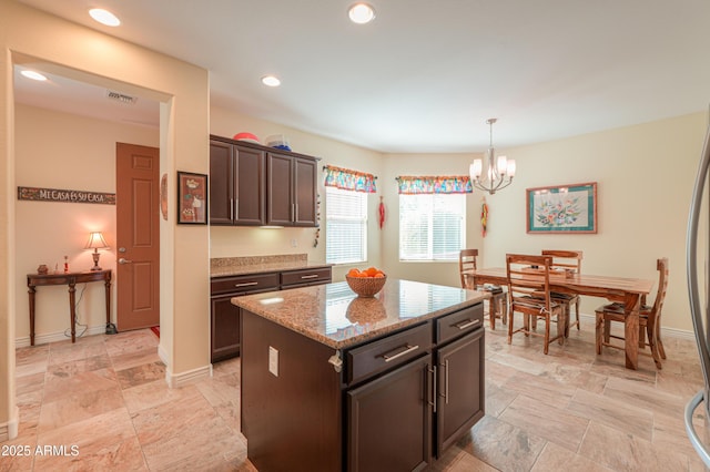 kitchen with light stone counters, a center island, a chandelier, dark brown cabinets, and hanging light fixtures