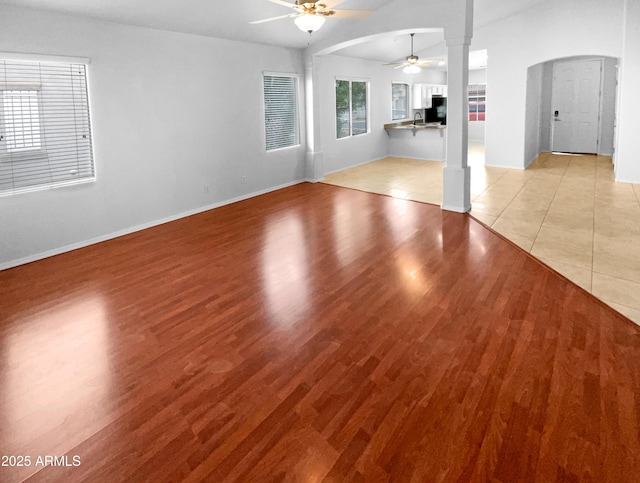 unfurnished living room featuring ornate columns, lofted ceiling, sink, ceiling fan, and light wood-type flooring