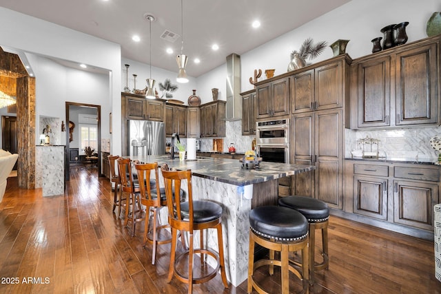 kitchen with dark wood-style flooring, dark countertops, visible vents, a towering ceiling, and appliances with stainless steel finishes