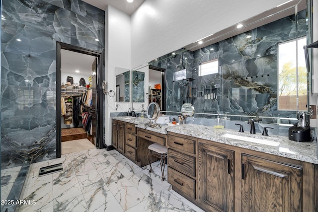 bathroom with marble finish floor, a spacious closet, double vanity, and a sink