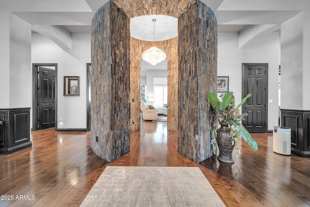 hall featuring arched walkways, a high ceiling, wood-type flooring, and a notable chandelier