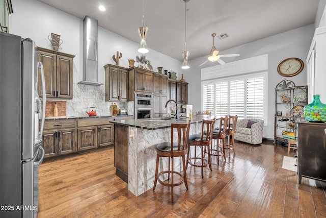 kitchen with tasteful backsplash, light wood-style flooring, appliances with stainless steel finishes, a breakfast bar, and wall chimney range hood