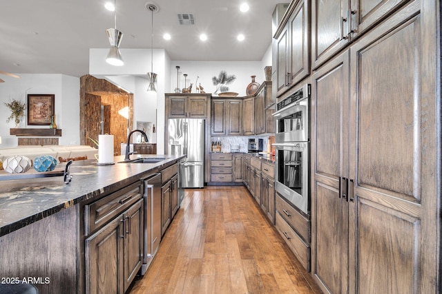 kitchen with stainless steel appliances, visible vents, hanging light fixtures, light wood-style flooring, and a sink