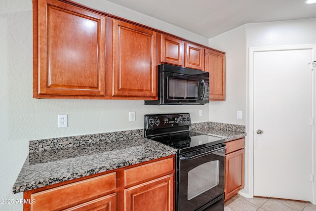 kitchen with light tile patterned floors, black appliances, dark stone countertops, and brown cabinetry