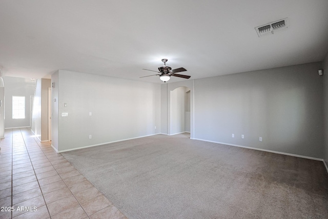 empty room featuring visible vents, light carpet, light tile patterned floors, arched walkways, and a ceiling fan