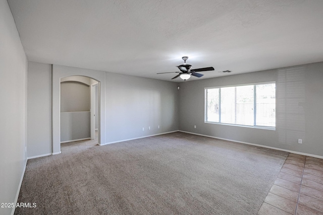 tiled empty room featuring visible vents, ceiling fan, baseboards, carpet, and arched walkways