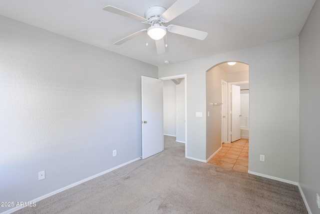 carpeted empty room featuring a ceiling fan, baseboards, and arched walkways