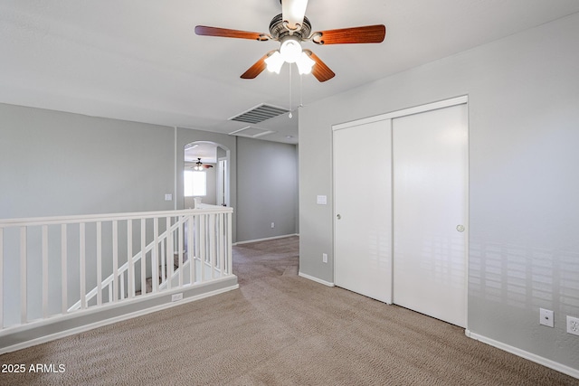 unfurnished bedroom featuring carpet, visible vents, arched walkways, ceiling fan, and a closet