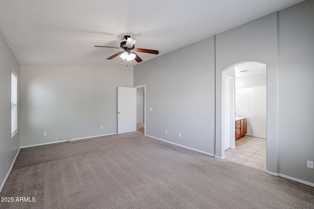 unfurnished room with light carpet, a ceiling fan, arched walkways, baseboards, and vaulted ceiling