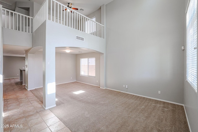 unfurnished living room featuring arched walkways, a high ceiling, light tile patterned floors, baseboards, and light colored carpet