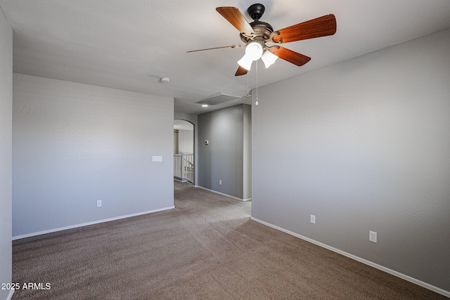 carpeted spare room with visible vents, arched walkways, baseboards, and ceiling fan