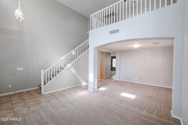 unfurnished living room featuring visible vents, carpet, stairway, a towering ceiling, and arched walkways