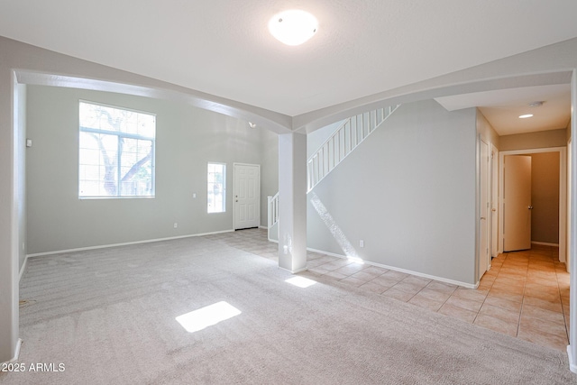 unfurnished living room with tile patterned floors, stairway, baseboards, and carpet