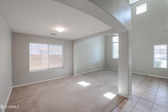 unfurnished room with light tile patterned floors, baseboards, visible vents, arched walkways, and light carpet