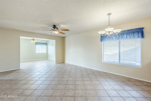 empty room featuring light tile patterned floors, ceiling fan with notable chandelier, baseboards, and a textured ceiling