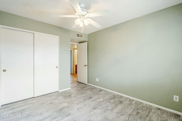 unfurnished bedroom with a closet, visible vents, a textured ceiling, and wood finished floors