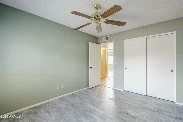 unfurnished bedroom featuring wood finished floors, visible vents, baseboards, a closet, and a textured ceiling