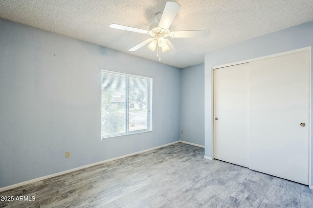 unfurnished bedroom with a closet, a textured ceiling, baseboards, and wood finished floors