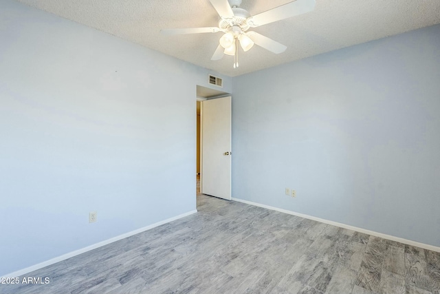 empty room featuring a ceiling fan, wood finished floors, visible vents, baseboards, and a textured ceiling