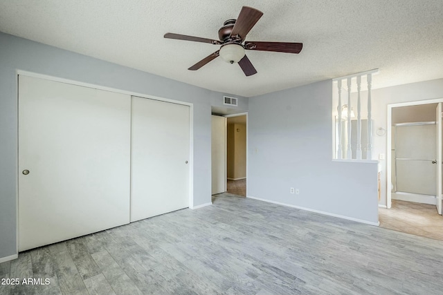 unfurnished bedroom featuring visible vents, baseboards, wood finished floors, a closet, and a textured ceiling