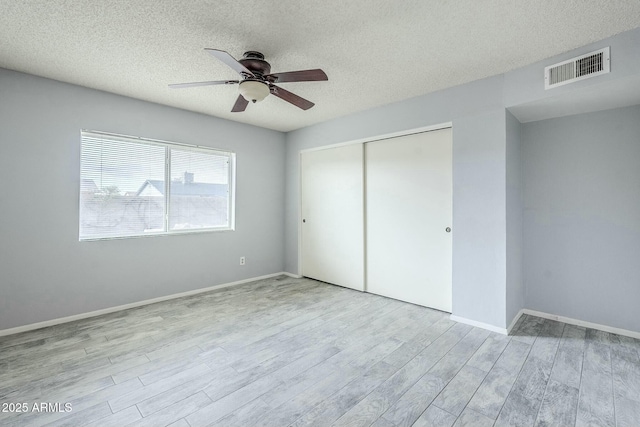 unfurnished bedroom featuring visible vents, a textured ceiling, wood finished floors, a closet, and baseboards