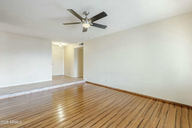 spare room with a ceiling fan, light wood-style floors, baseboards, and a textured ceiling