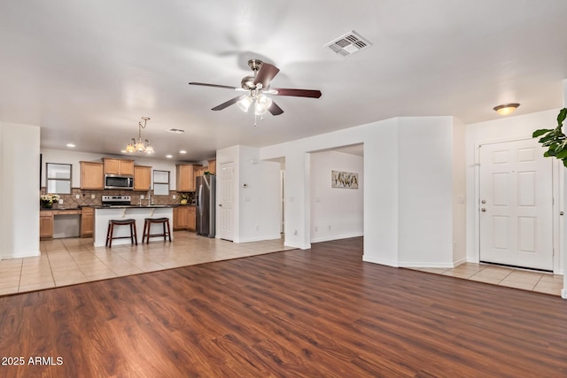 unfurnished living room with baseboards, ceiling fan with notable chandelier, visible vents, light wood-style floors, and recessed lighting