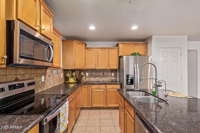 kitchen with tasteful backsplash, appliances with stainless steel finishes, dark stone countertops, a sink, and light tile patterned floors