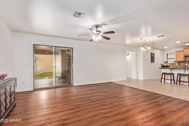 living room featuring ceiling fan with notable chandelier, visible vents, and wood finished floors