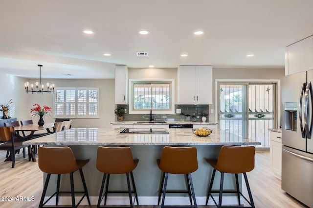 kitchen featuring white cabinetry, an inviting chandelier, light stone counters, stainless steel fridge, and decorative light fixtures