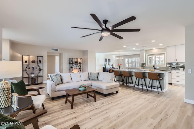 living room featuring sink, light hardwood / wood-style floors, and ceiling fan with notable chandelier