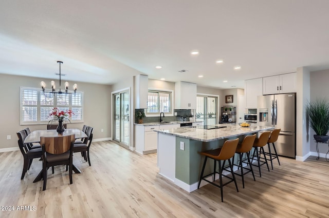 kitchen featuring white cabinetry, a center island, hanging light fixtures, stainless steel fridge with ice dispenser, and light wood-type flooring