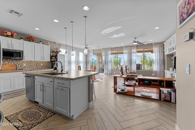 kitchen featuring sink, light parquet flooring, ceiling fan, stainless steel appliances, and a center island with sink