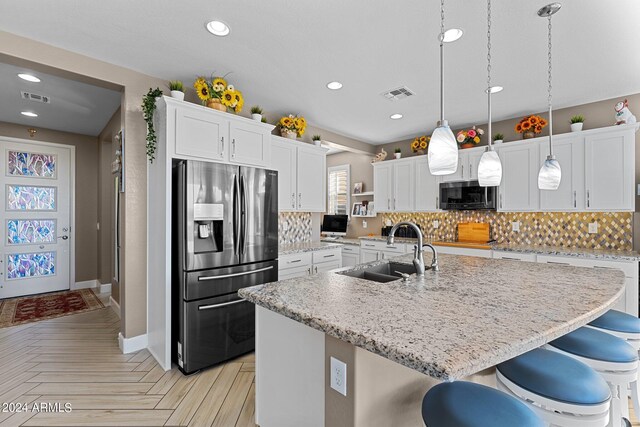 kitchen featuring white cabinetry, sink, stainless steel appliances, light parquet flooring, and a center island with sink