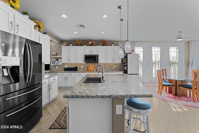 kitchen with black fridge with ice dispenser, sink, a center island with sink, light stone countertops, and white cabinets