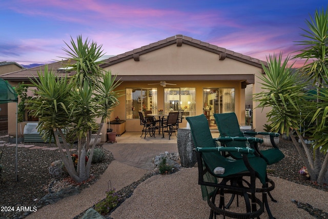 back house at dusk featuring a patio area and ceiling fan