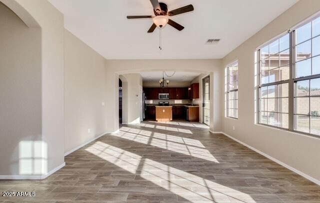 15105 W Glenrosa Ave, Goodyear, AZ 85395 - unfurnished living room featuring arched walkways, baseboards, a ceiling fan, and light wood-style flooring