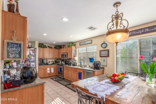 kitchen with appliances with stainless steel finishes, light tile patterned floors, sink, and pendant lighting